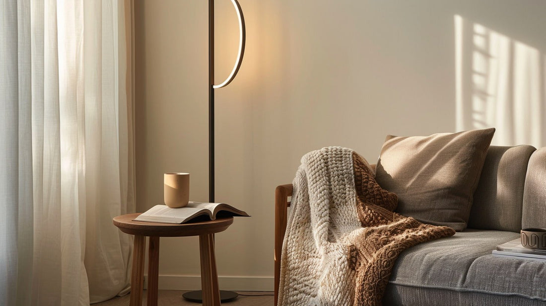 A soft-lit living room scene with a sofa, a knit blanket, a small round side table with an open book and mug, and a slim floor lamp near sheer curtains. A soft-lit living room scene with a sofa, a knit blanket, a small round side table with an open book and mug, and a slim floor lamp near sheer curtains.